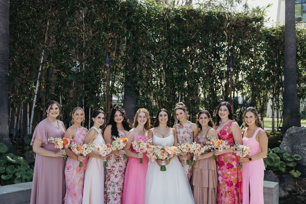 Outdoor wedding party photo with bridesmaids in coordinated pink and floral dresses.