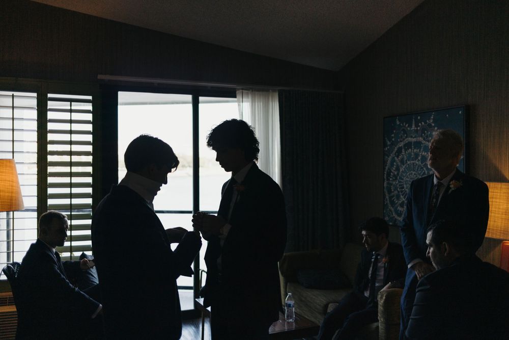 Silhouettes of people gathered in a dimly lit room with window light and lamp creating atmospheric shadows.