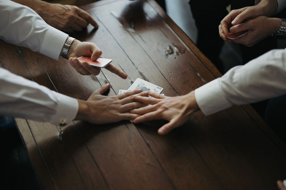 Multiple hands reaching across a wooden table in a dramatic overhead shot.