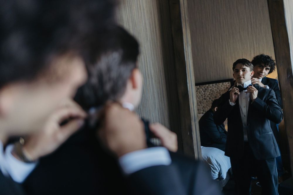 Reflection in mirror shows formal preparation scene with dark suits and ambient lighting.