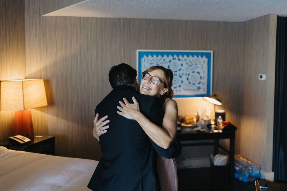 Emotional embrace in hotel room with warm lamp lighting and blue wall art.