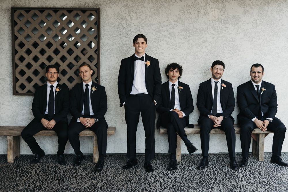 Wedding party in suits posed casually against wall with decorative lattice pattern.