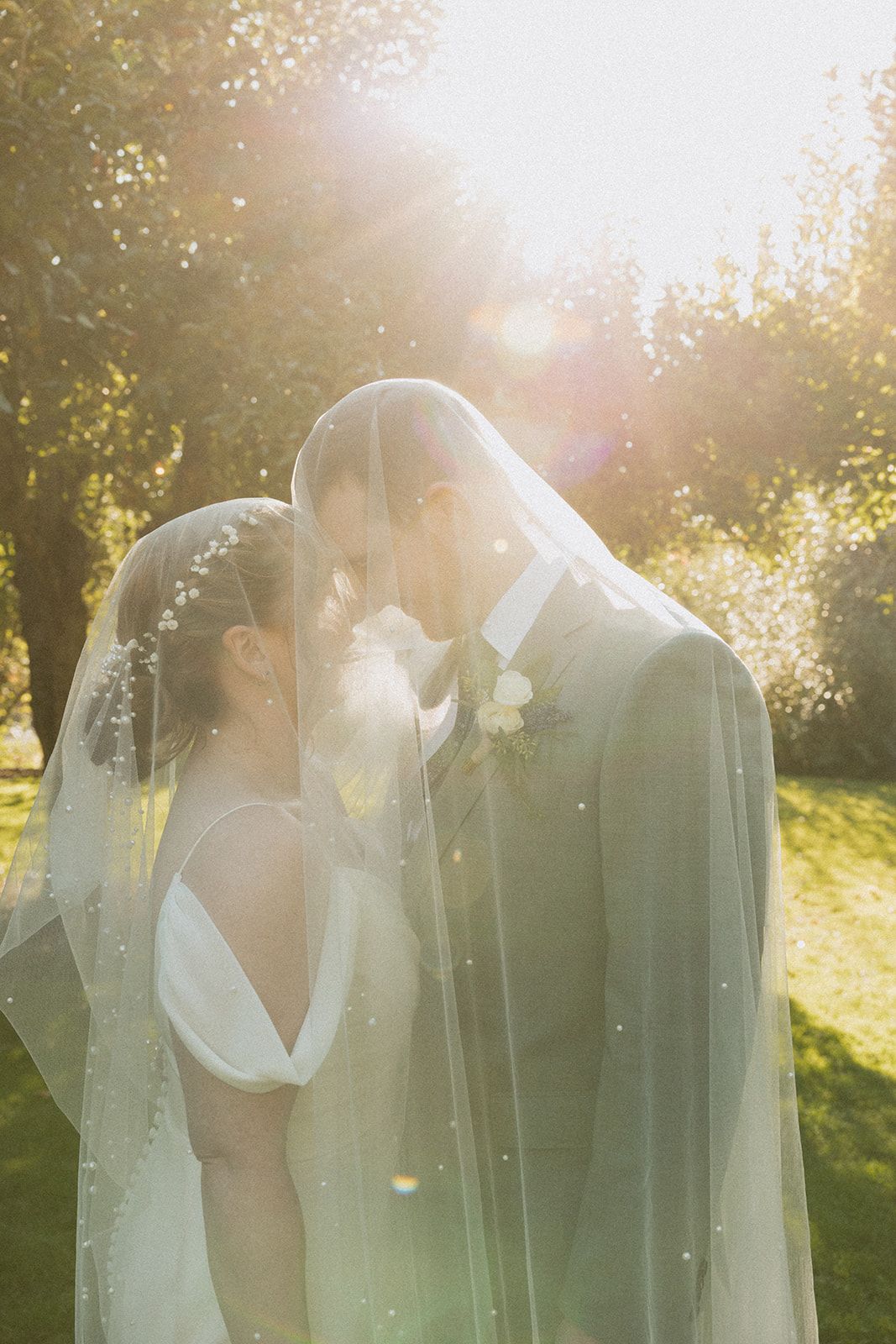 Dreamy backlit wedding photo with sunflares filtering through a delicate veil.