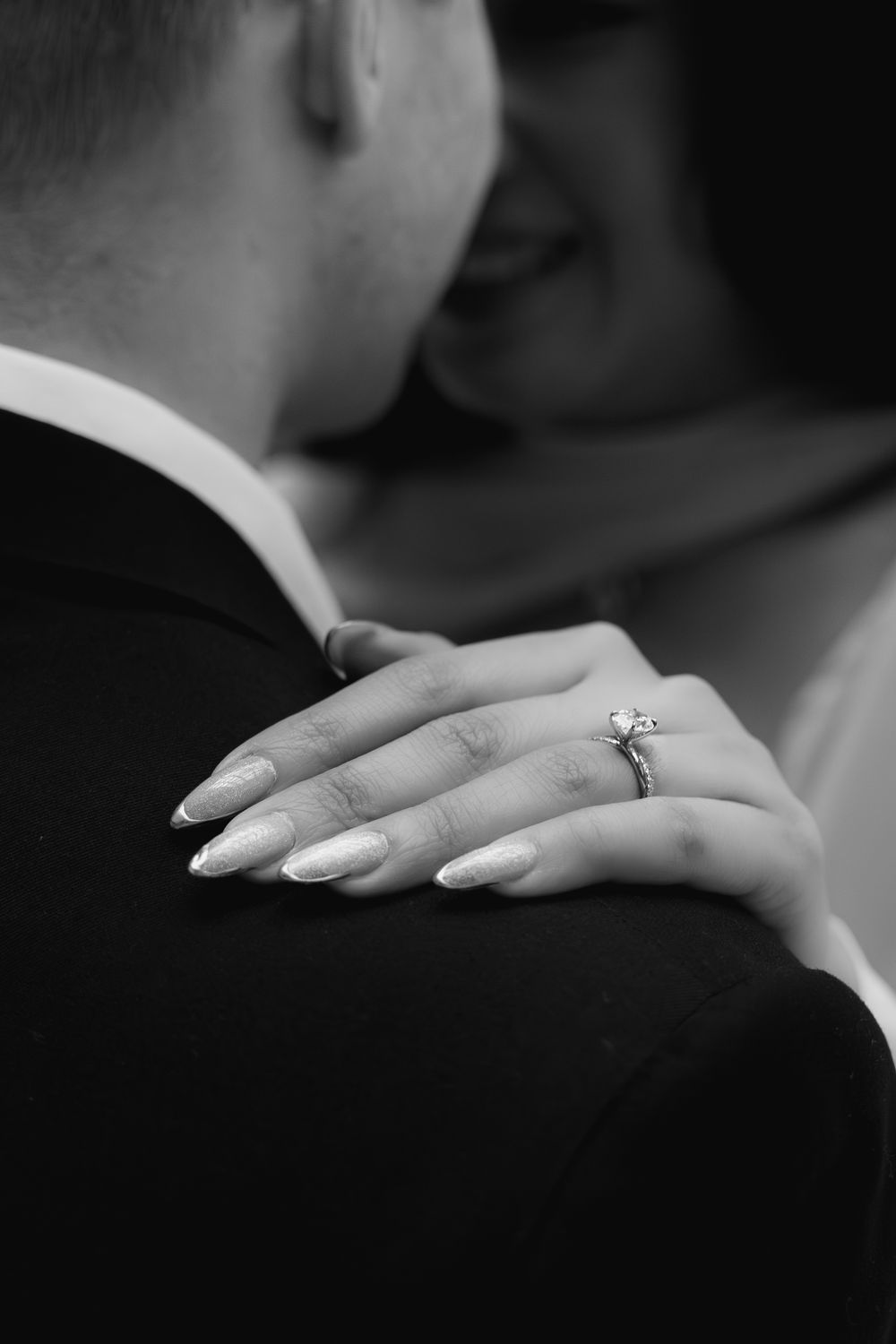 Black and white close-up of two hands wearing wedding rings in an intimate romantic moment.