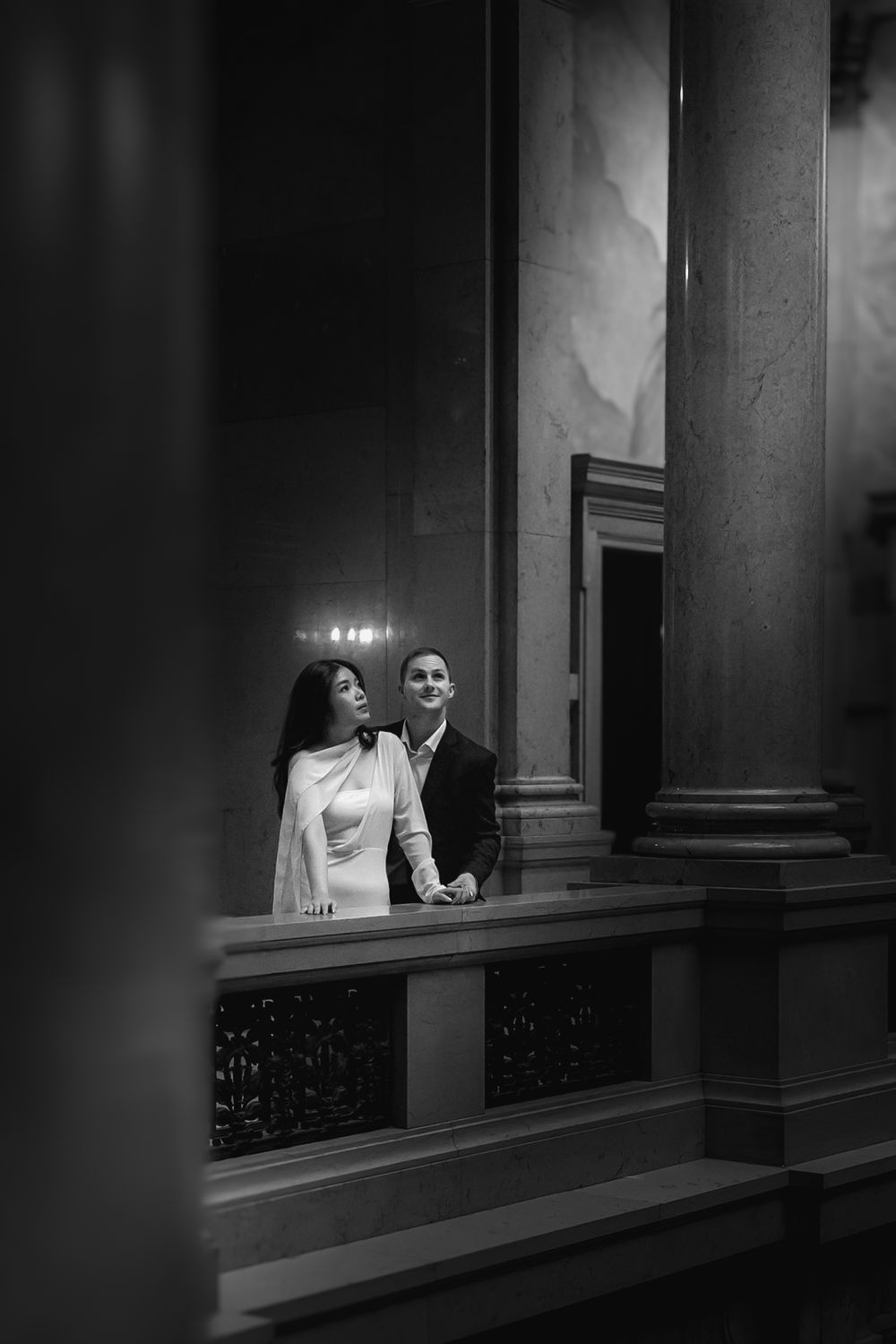 A dramatic black and white series showing a couple on a balcony with moody architectural lighting and columns.