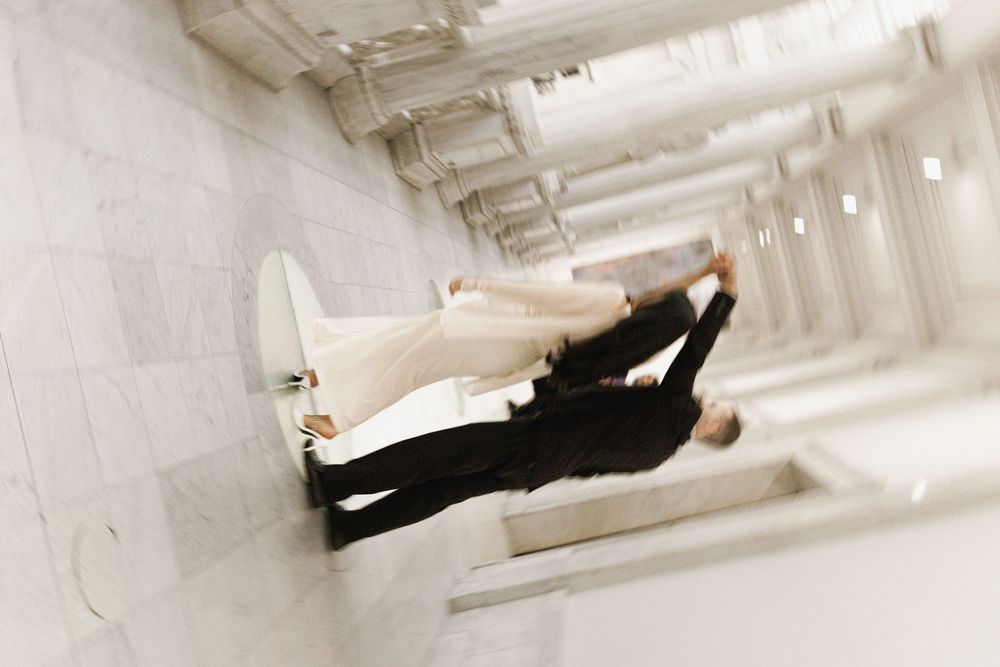 Wedding couple walking through bright industrial hallway with white walls and ceiling lights.