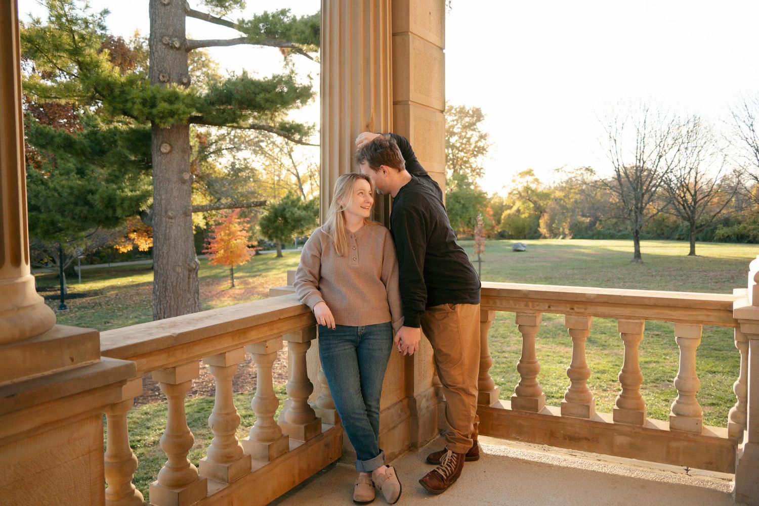 Couple sharing romantic moment on stone balcony surrounded by autumn landscape.