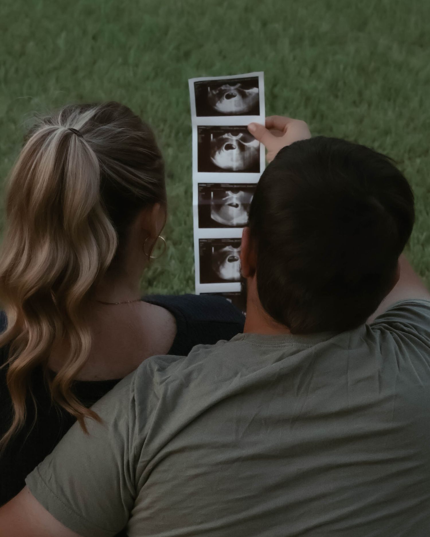 Couple embracing while looking at ultrasound photos in a park setting.