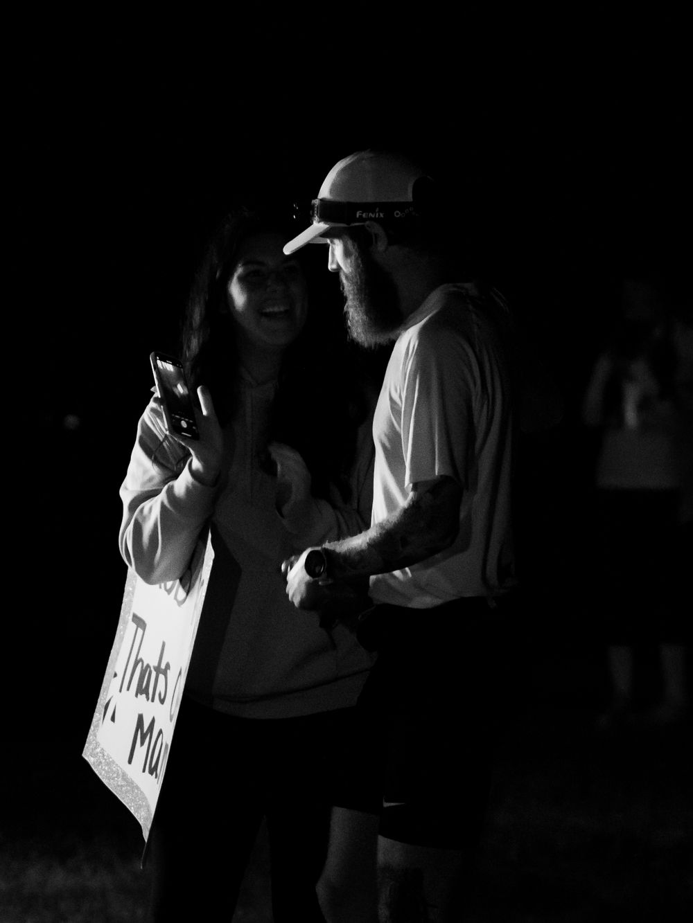 Black and white photo of runners checking phones at nighttime race event.