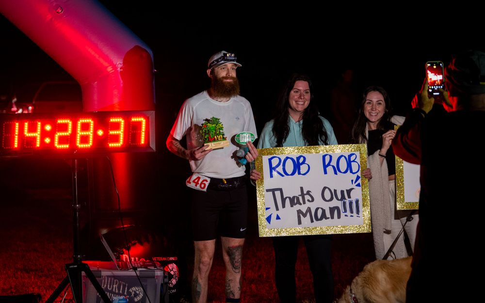 A nighttime scene with red lighting and spectators holding signs near a digital clock display.