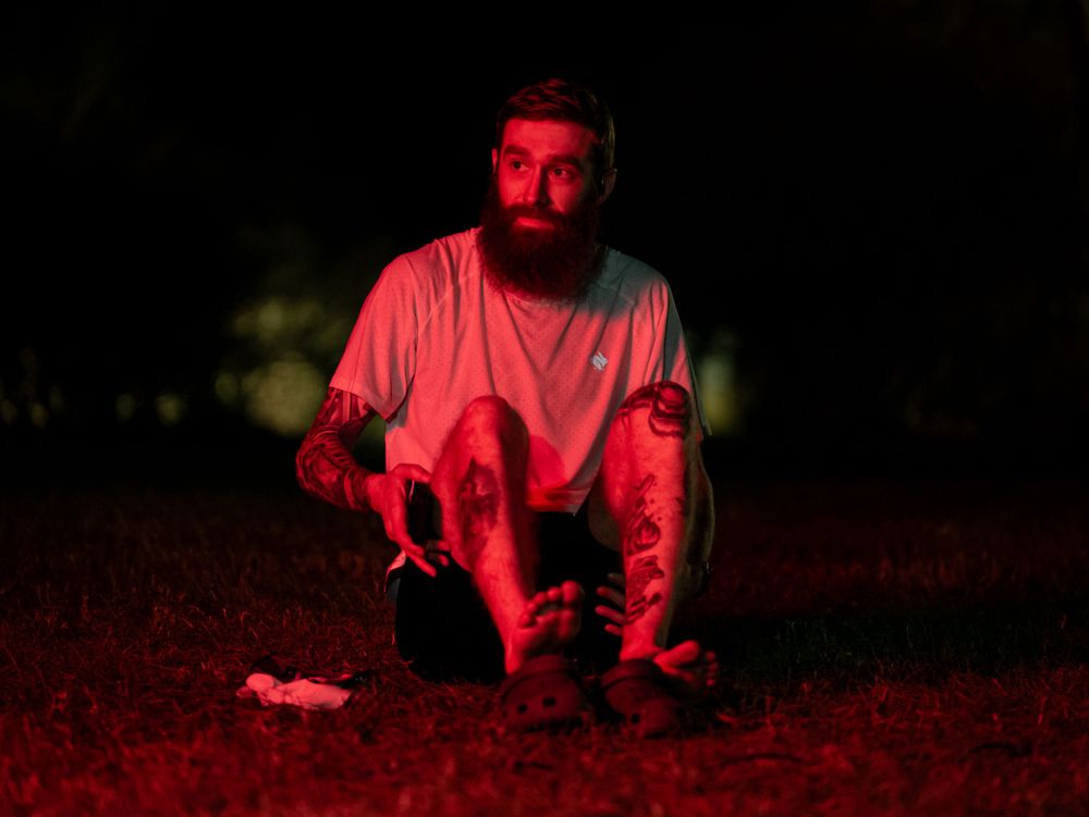 A figure bathed in red light crouching outdoors at night.