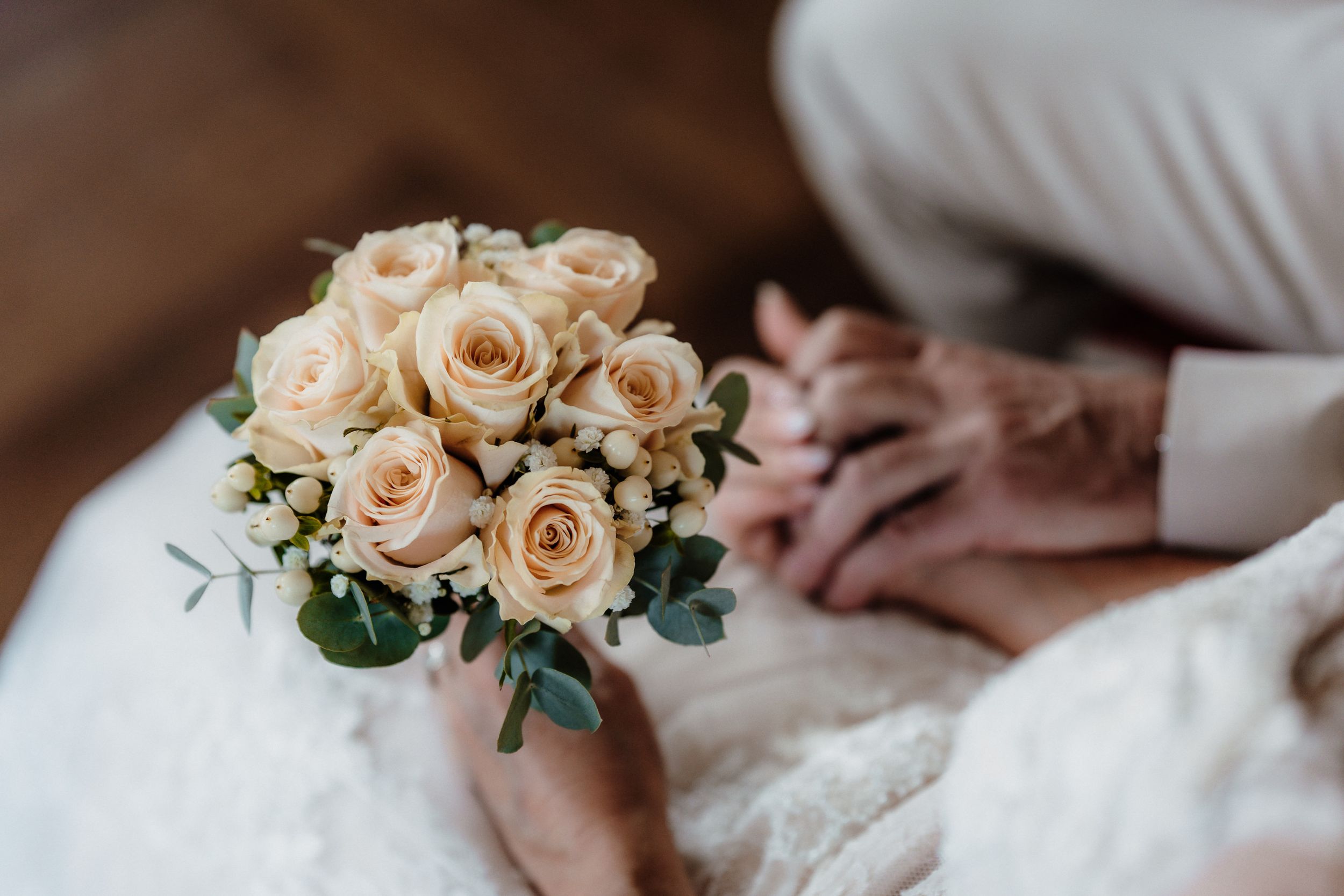 Delicate peach rose wedding bouquet held against white dress fabric.