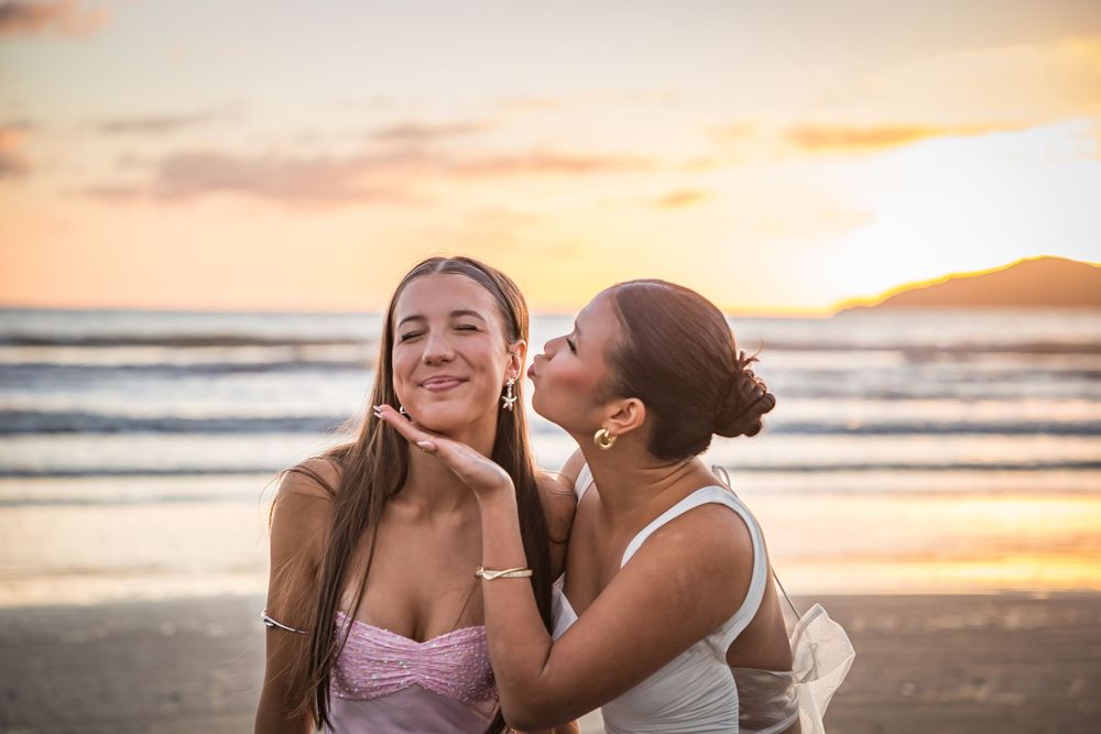 Two friends sharing a joyful moment at the beach during golden hour sunset with ocean waves in the background.