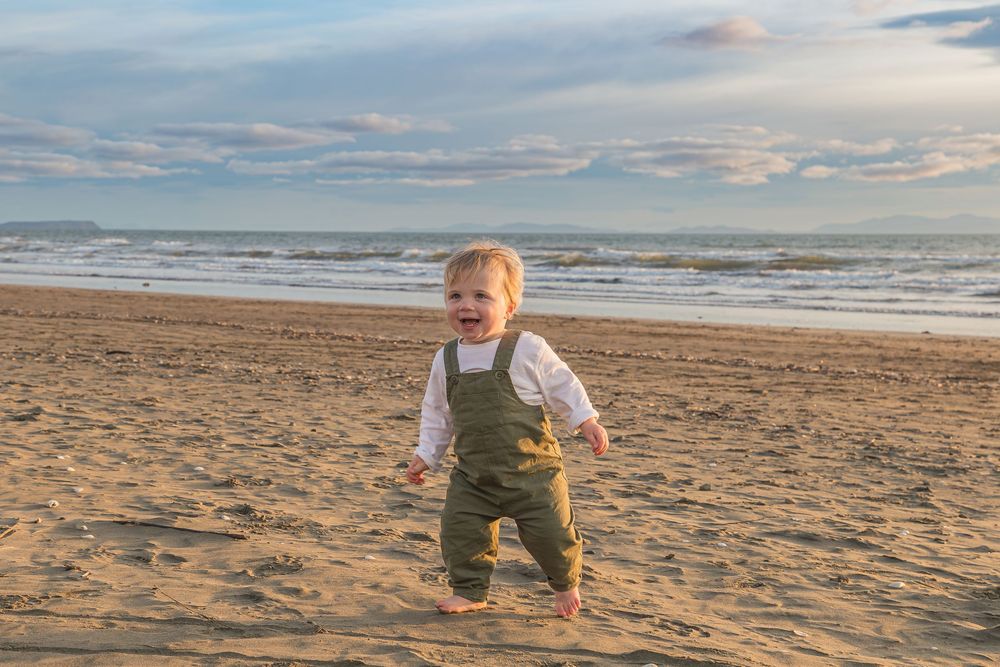 A child runs and plays along a sandy beach at sunset with waves rolling in from the ocean.