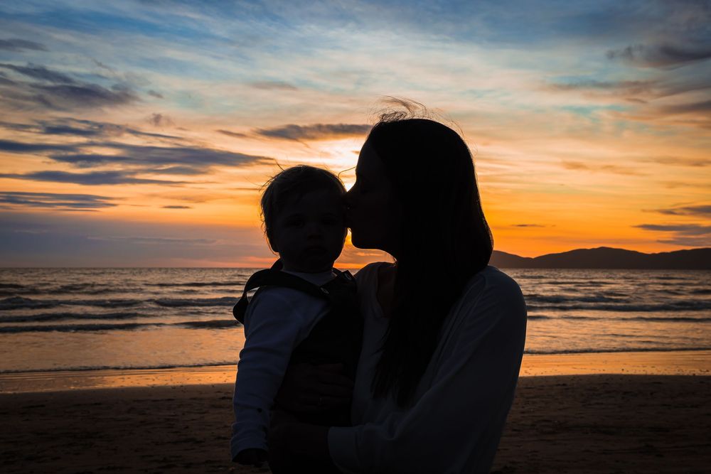 Silhouettes embrace on a beach at sunset with dramatic orange sky and ocean waves in the background.
