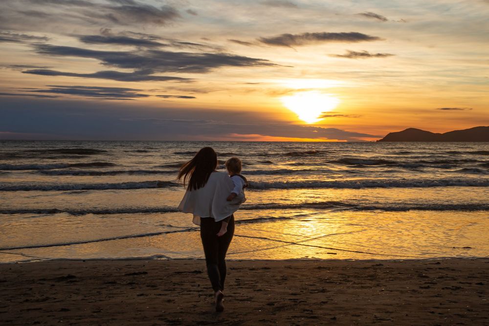 A series of silhouettes walking along a beach at sunset with golden light reflecting on the ocean waves.