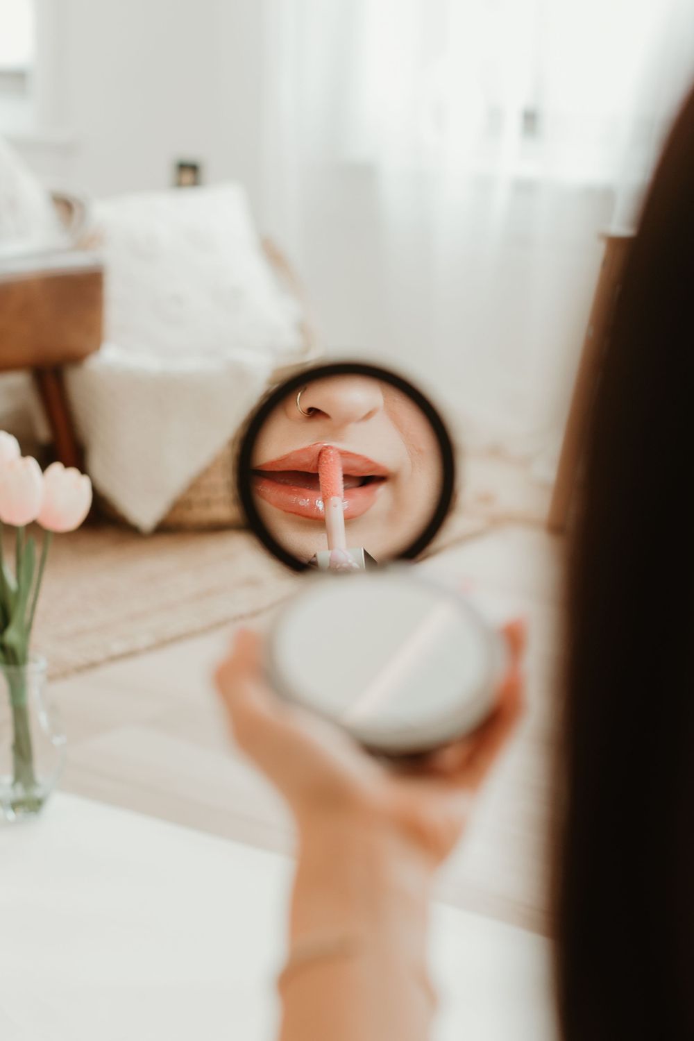 Reflection in handheld mirror showing application of pink lipstick.
