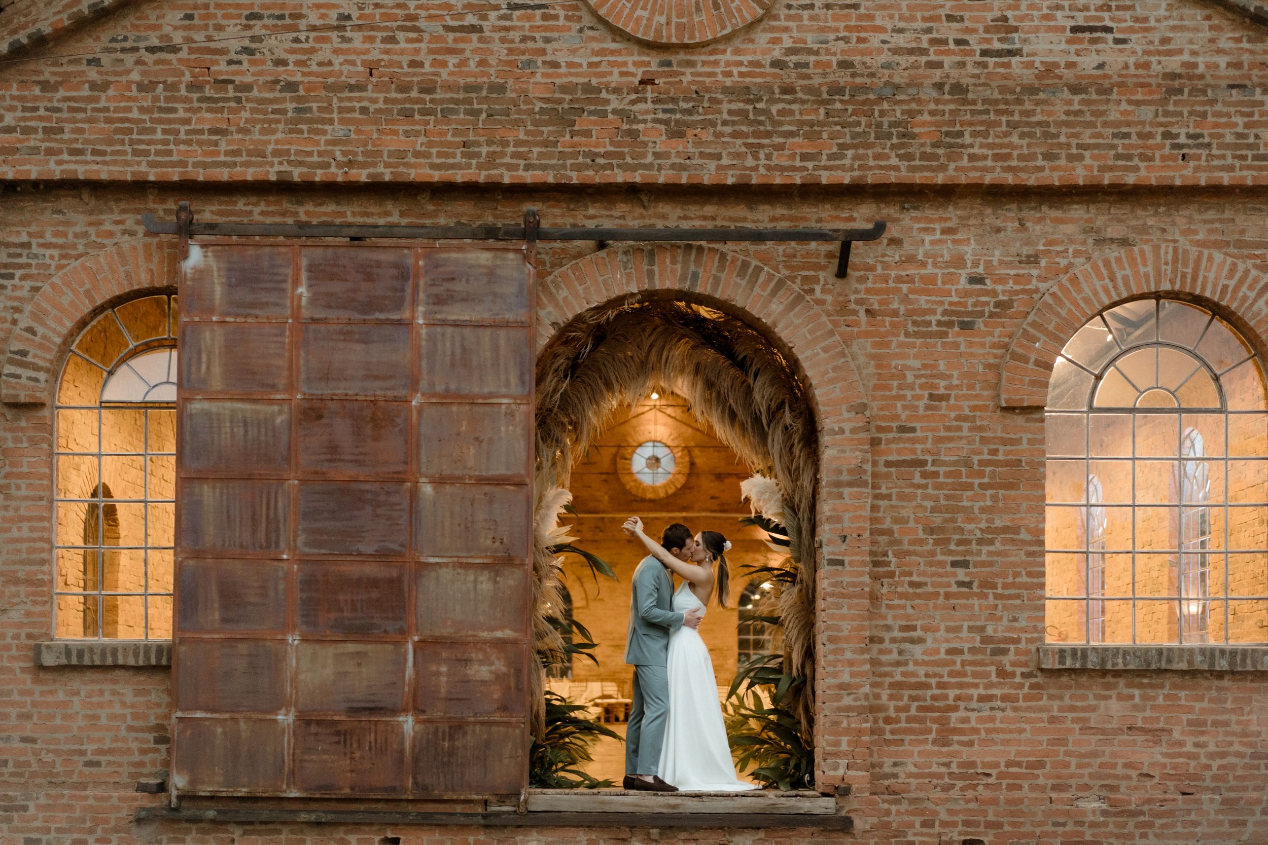 A wedding couple silhouetted in an illuminated brick archway at dusk.