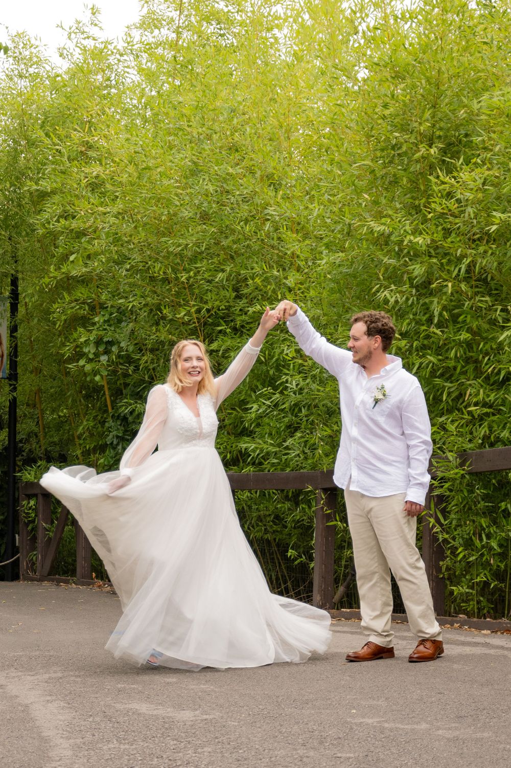A wedding couple shares a romantic dance pose on a pathway surrounded by lush green bamboo vegetation.