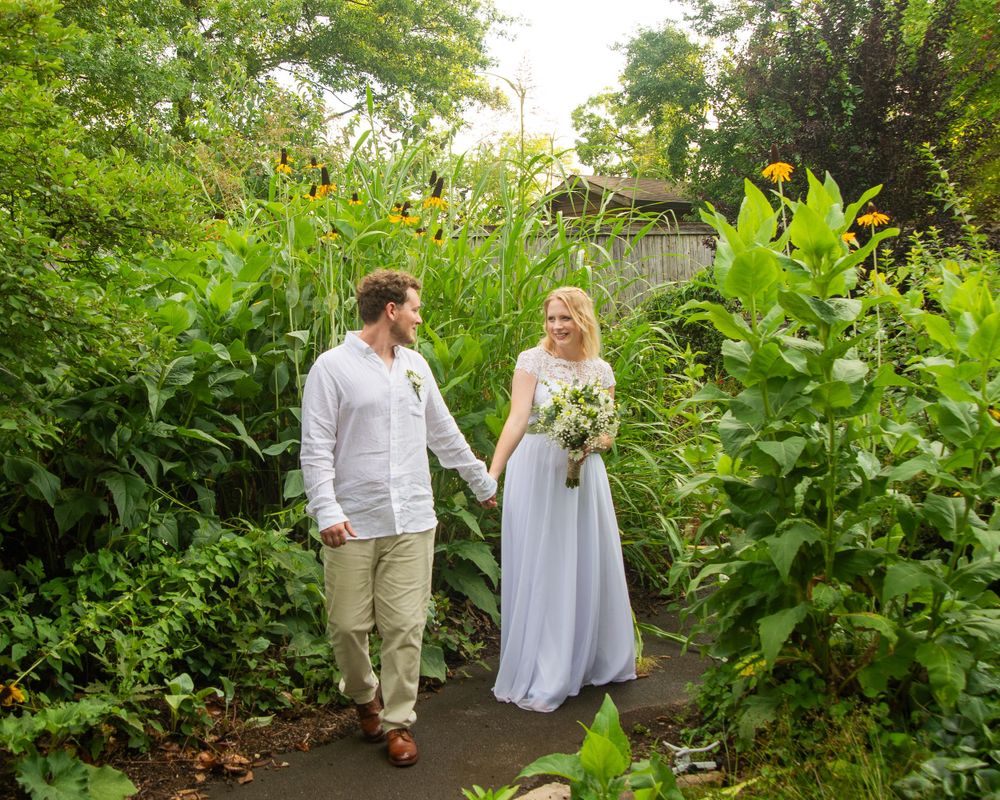 A couple walking hand in hand through a garden path filled with colorful flowers and greenery.