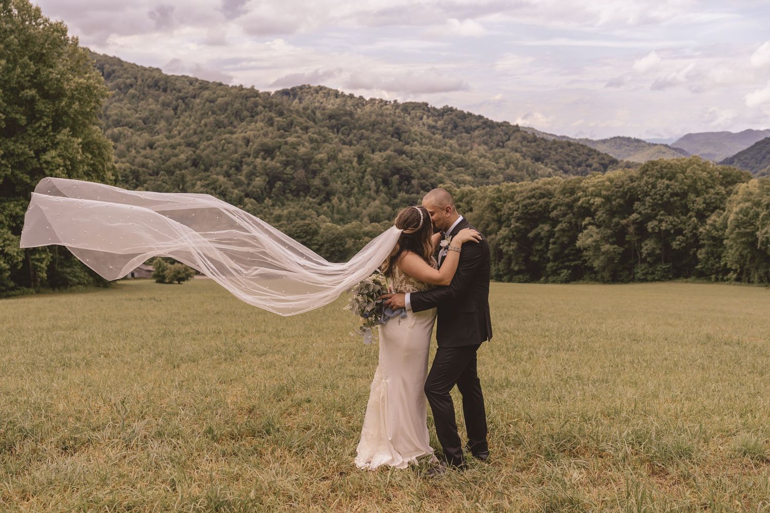 Bride and groom kissing with flowing veil and mountain views at The Heavens Venue in Hot Springs, NC