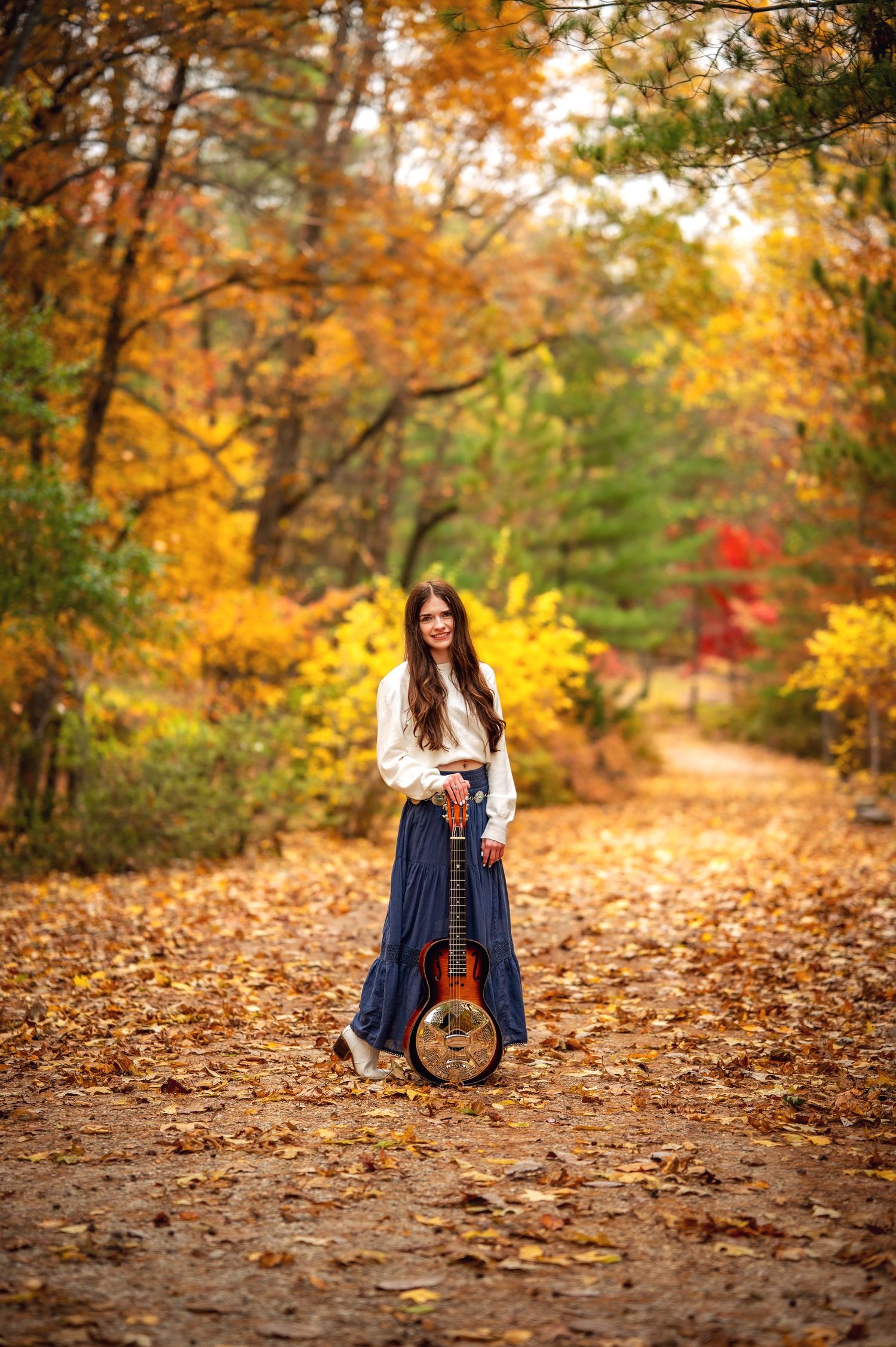 Autumn forest path covered in fallen golden leaves with vibrant orange foliage overhead creates a warm seasonal scene.
