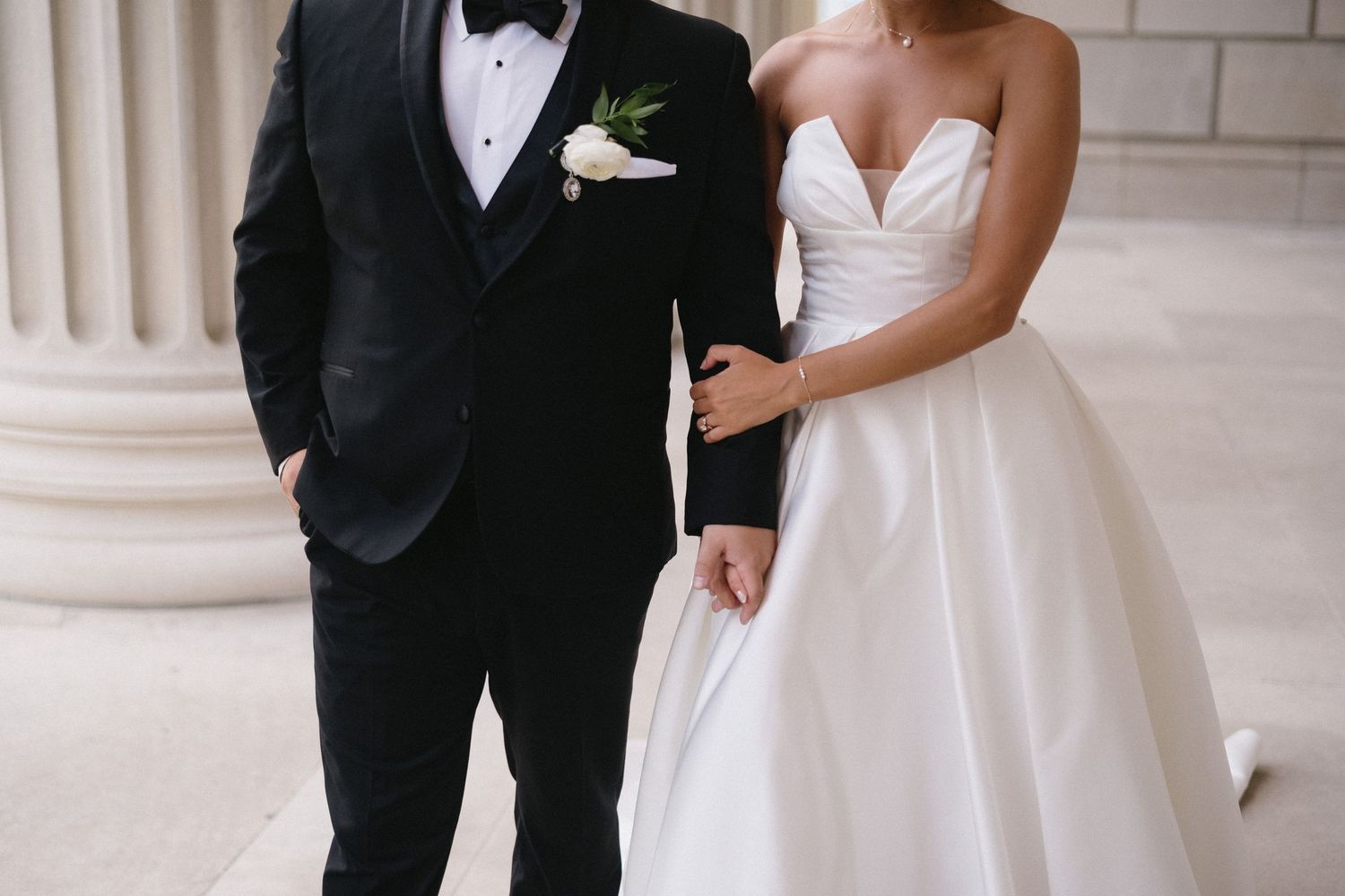 Wedding couple in formal attire posing in front of classical stone columns.