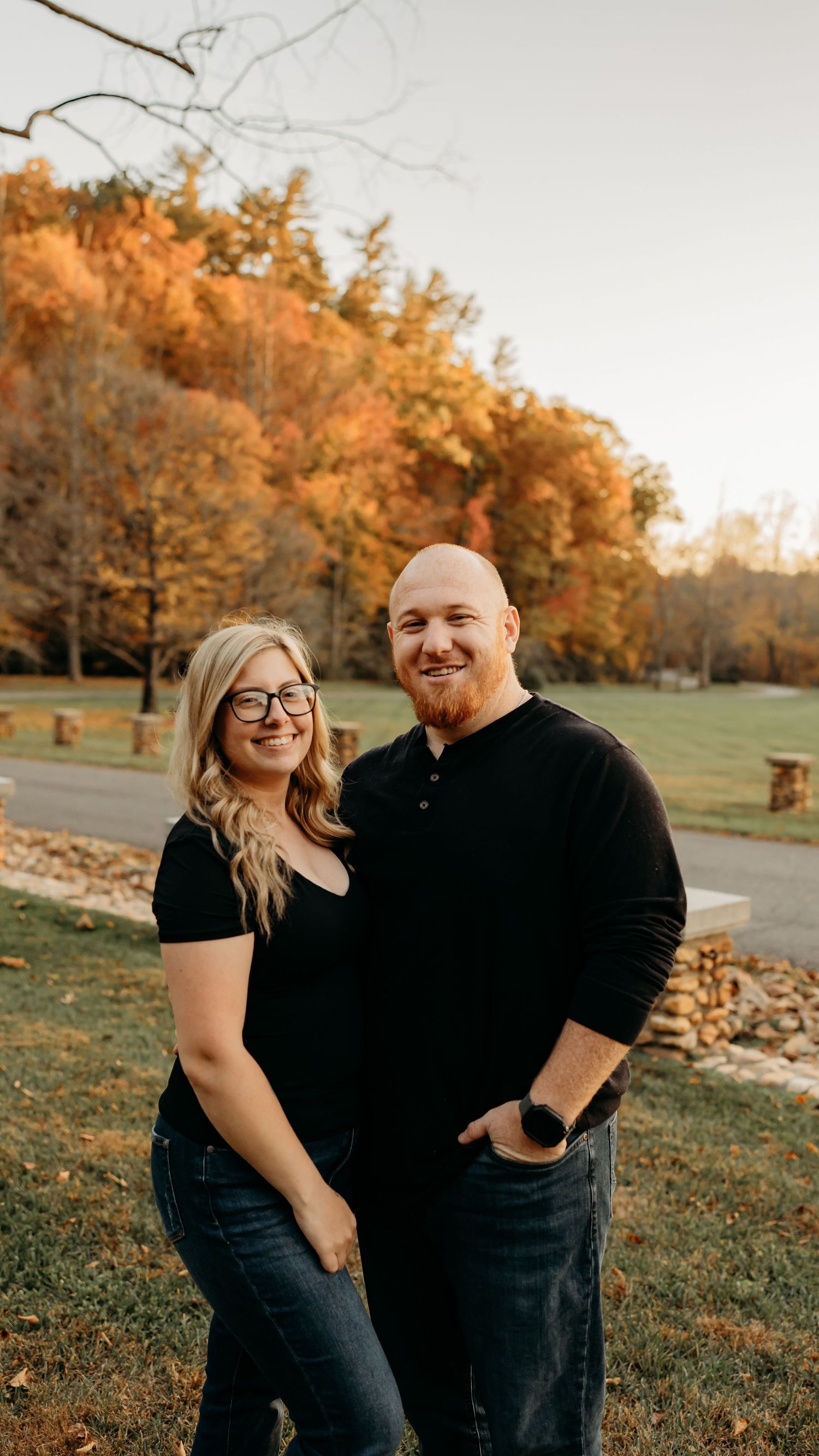Couple posing outdoors during golden hour with fall foliage in the background.