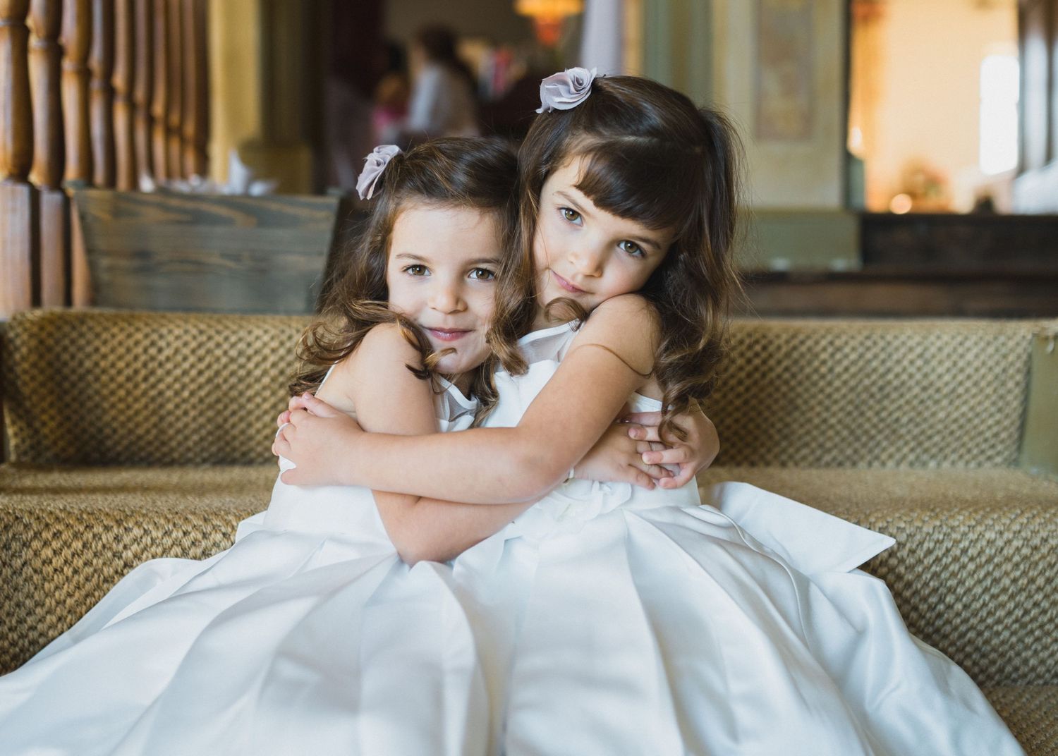 Two young girls in white dresses embrace while sitting together on staircase with Nova Scotia wedding photographer.