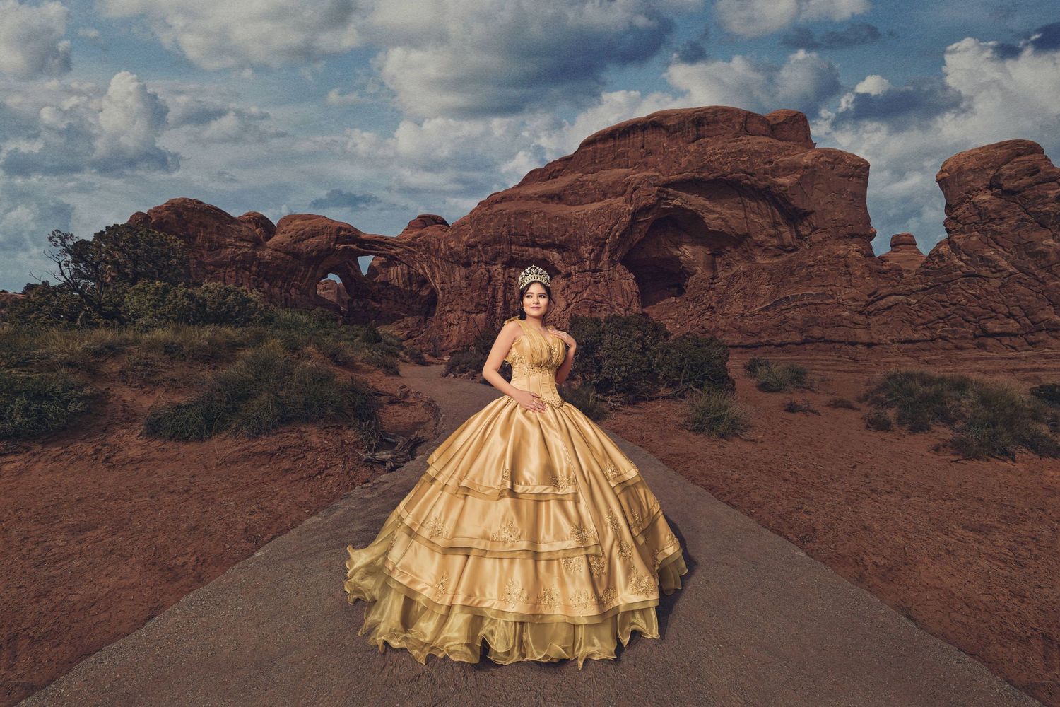 A gold ball gown dress stands out against the dramatic red rock formations and desert landscape of Arches National Park.