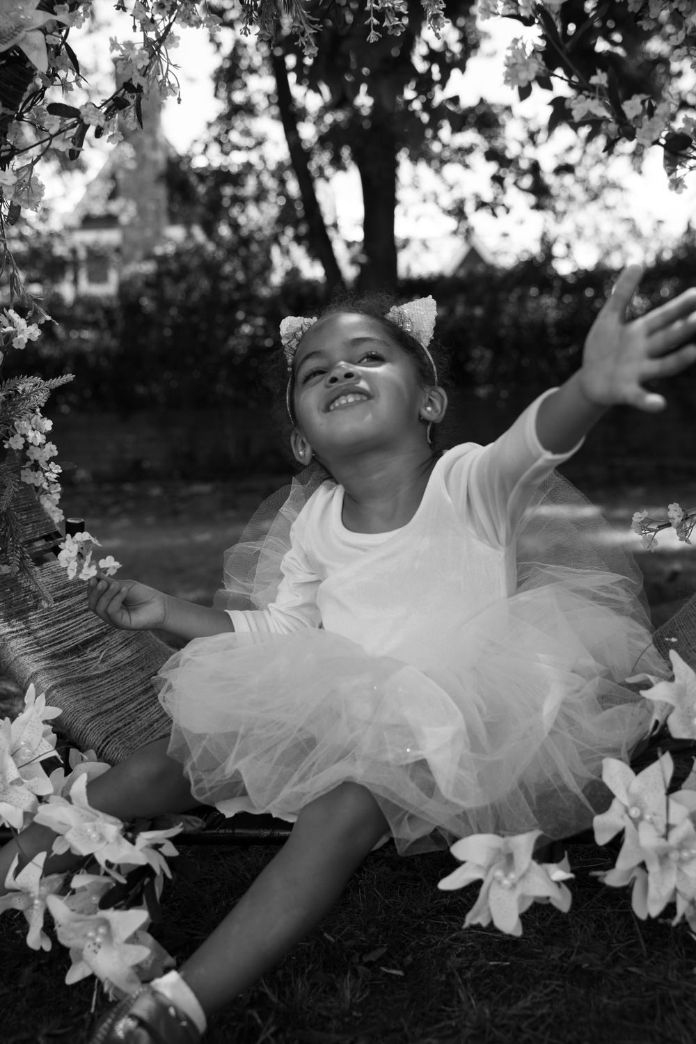 A young dancer in a white tutu poses joyfully among flowers in a black and white photo.