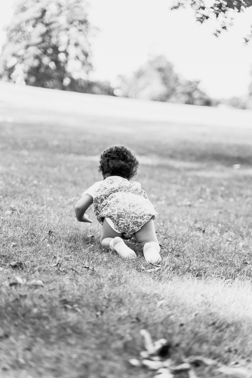 A toddler crawls on grass in black and white, wearing a patterned outfit.