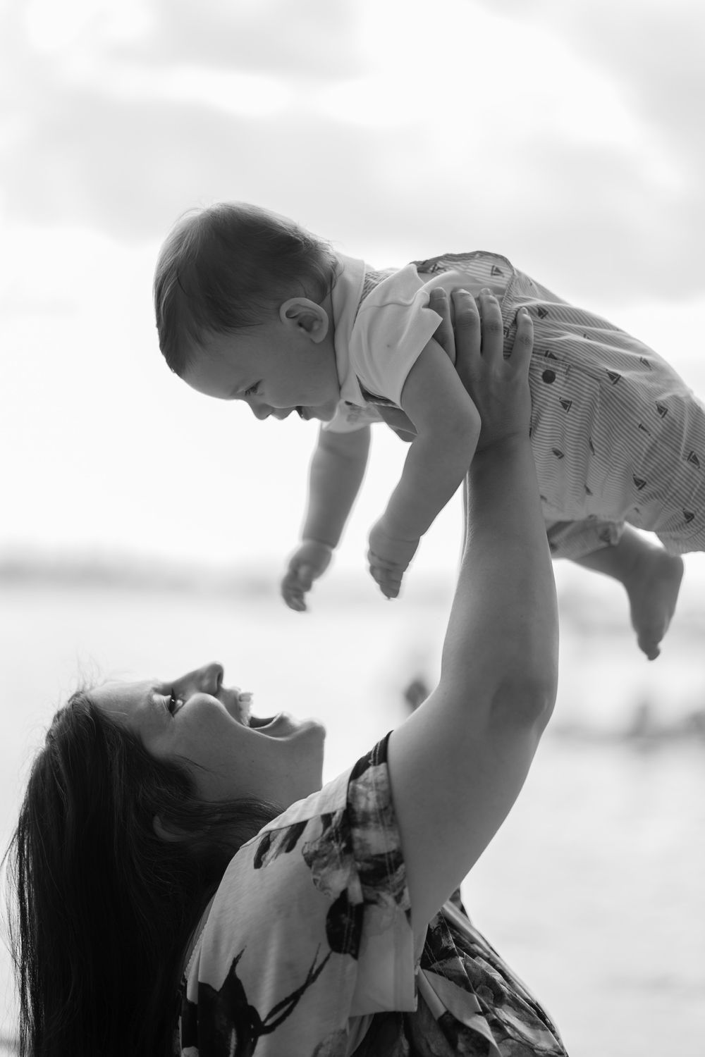 A tender moment captured in black and white as a parent lifts a baby high into the air.