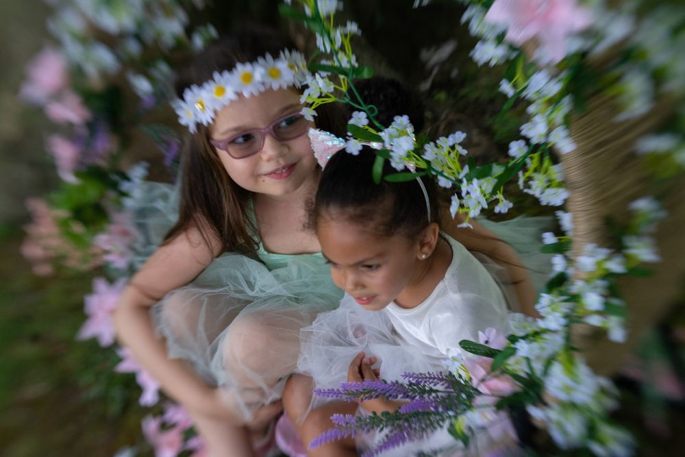 Two children wearing flower crowns share a tender moment among spring blossoms.