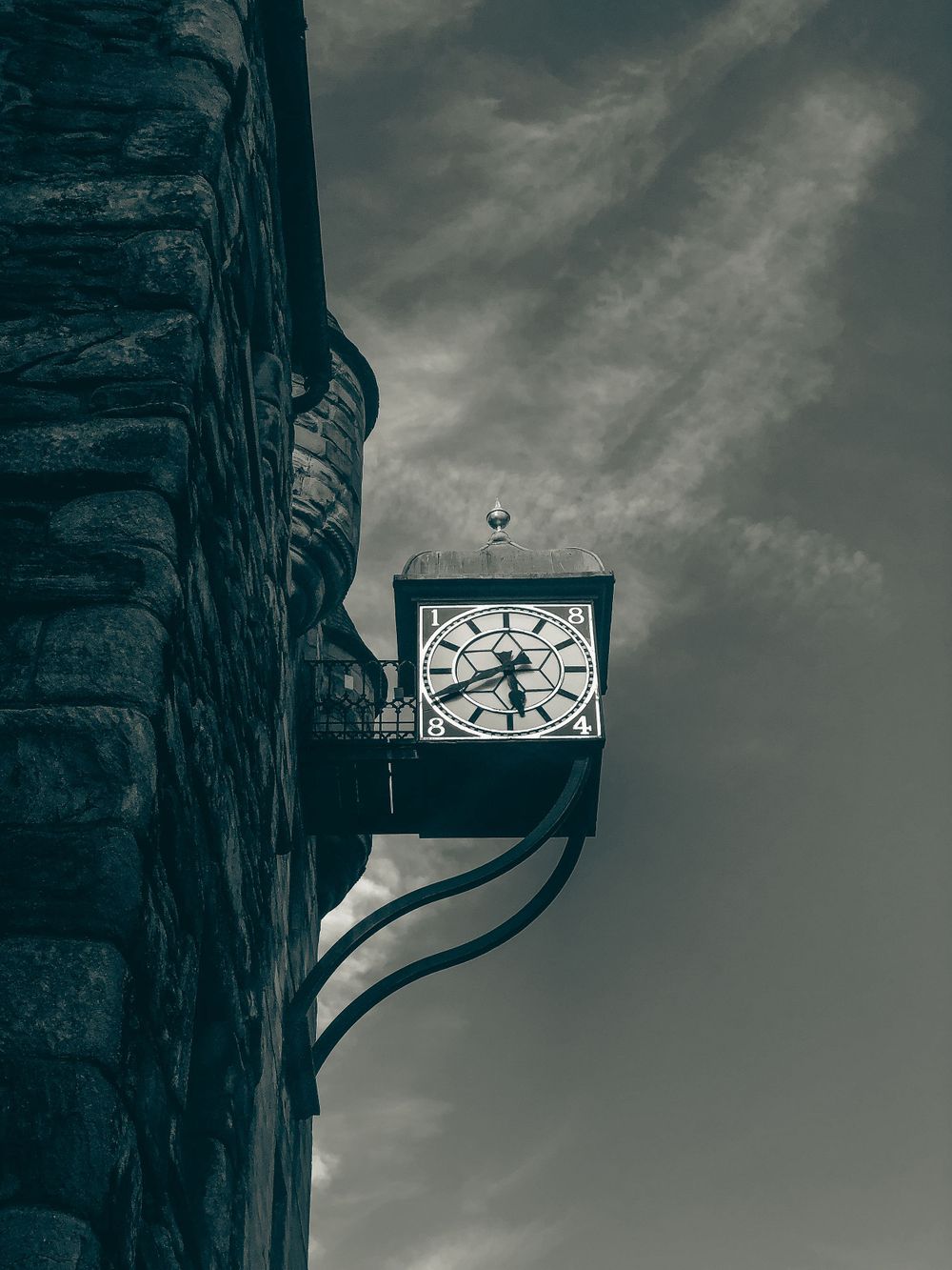 A vintage clock mounted on a stone wall against a moody gray sky.