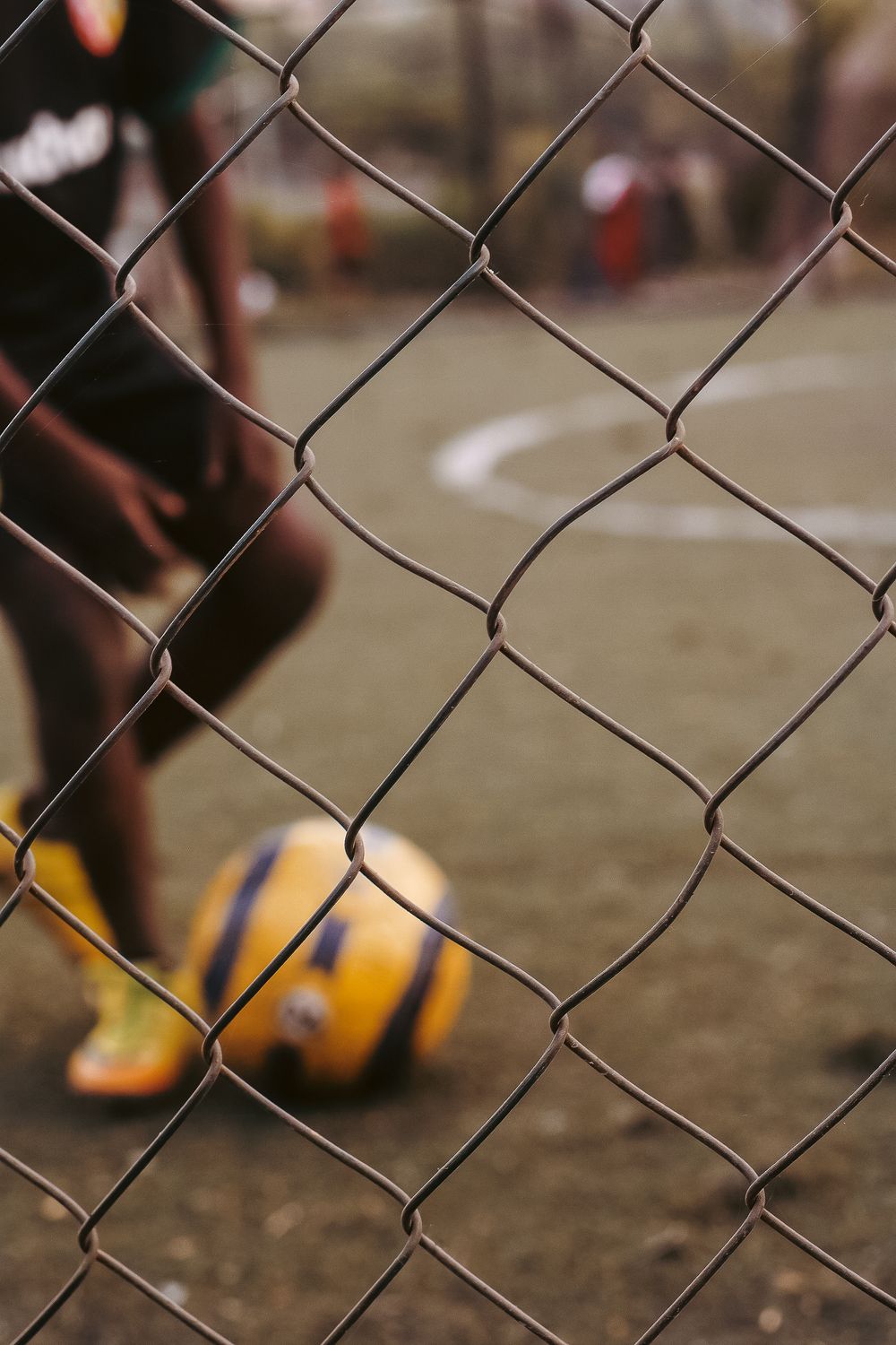 Soccer ball visible through chain link fence on a sports field showing focused depth of field.