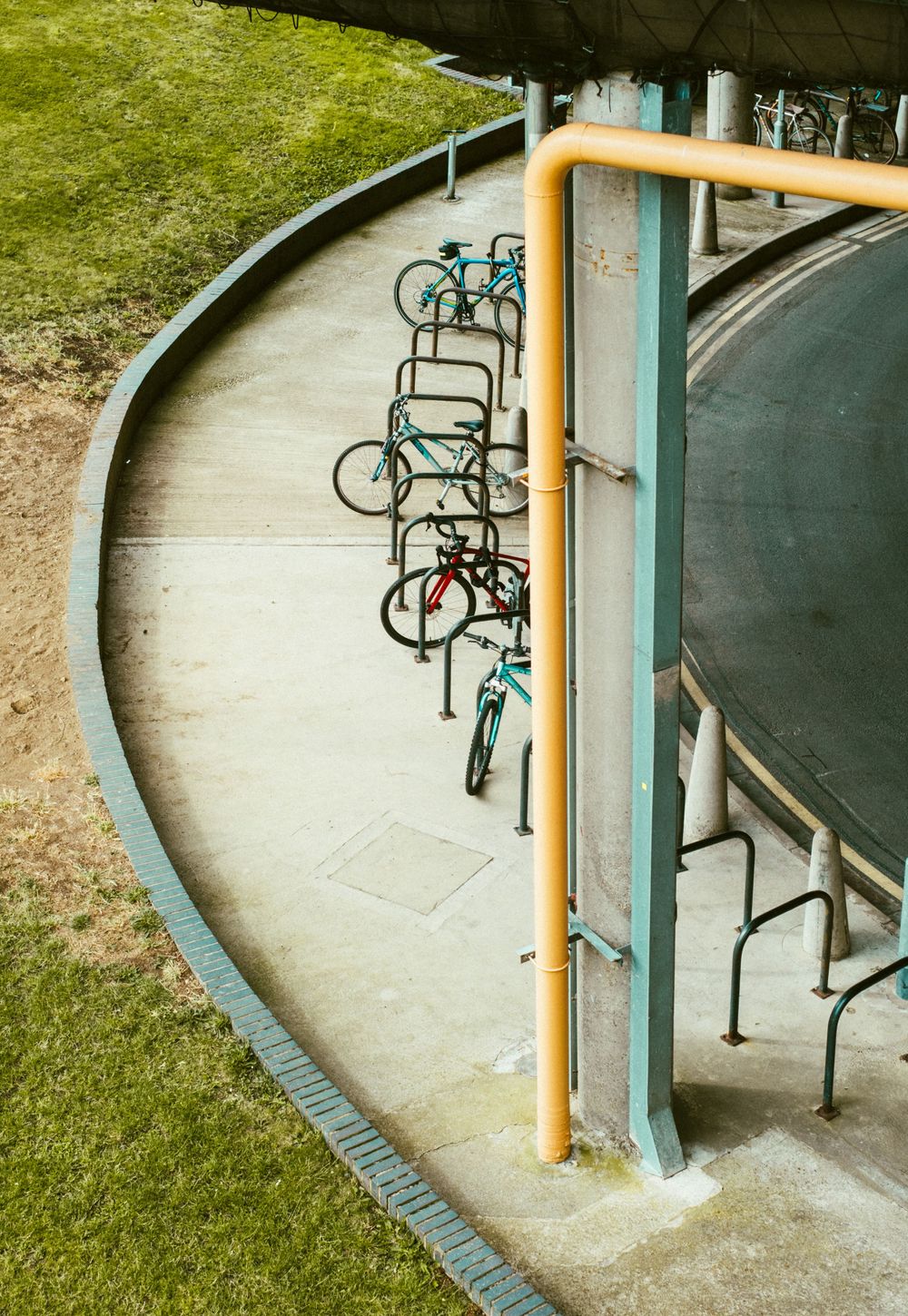 A curved concrete walkway with bike racks installed along the wall and green grass visible in the background.