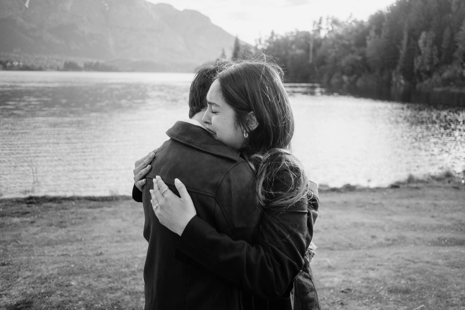 Abrazo emotivo tras una pedida de mano sorpresa a orillas del Lago Moreno, Bariloche. Fotografía documental de pareja.