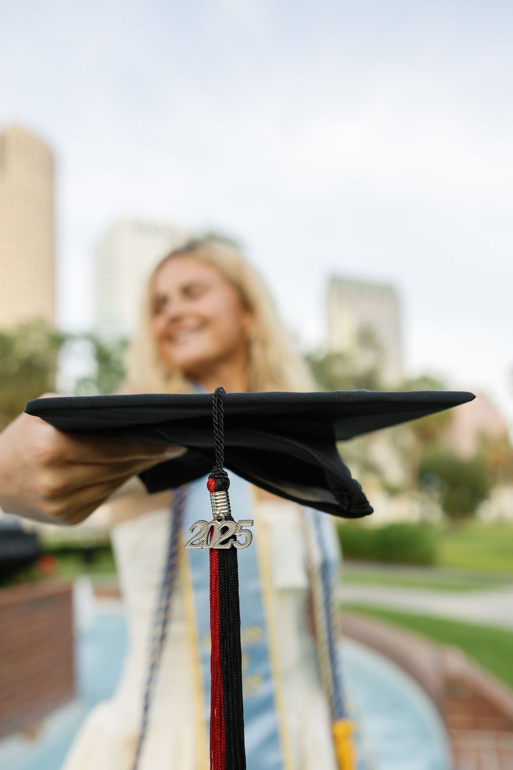 A graduation cap with 2023 tassel shown in focus against a blurred outdoor background with city buildings.