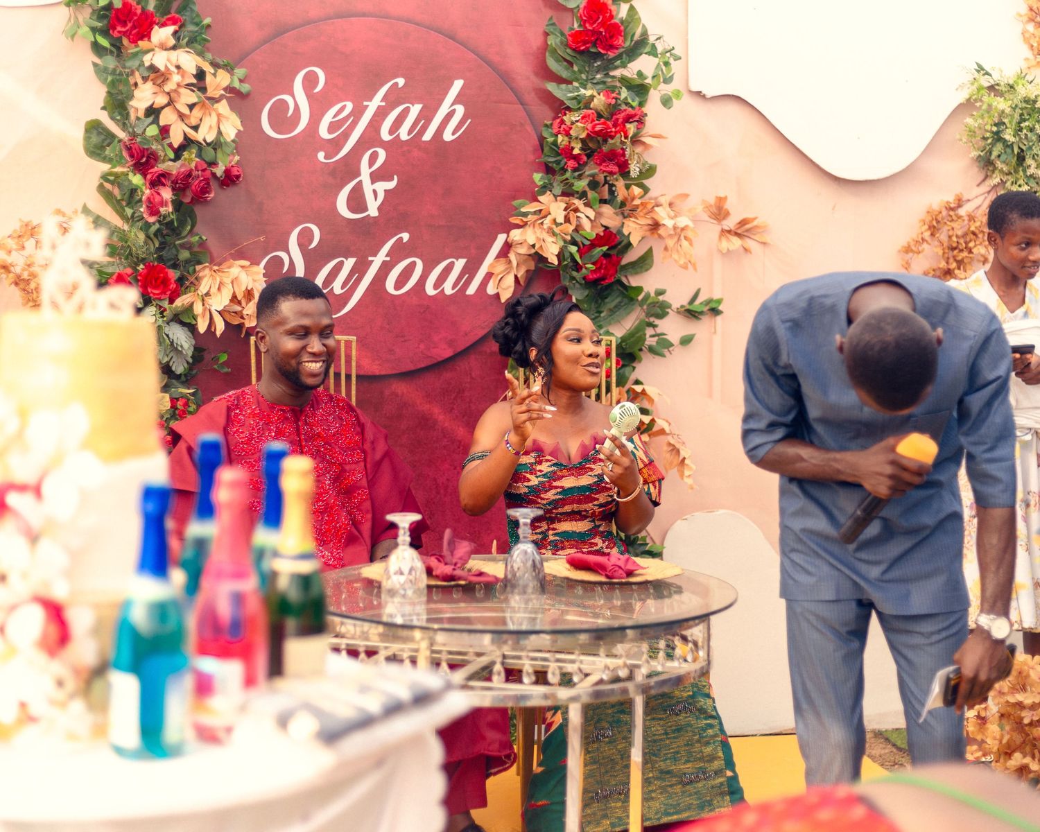 Traditional ceremony setup with floral arch and refreshment table against coral wall.