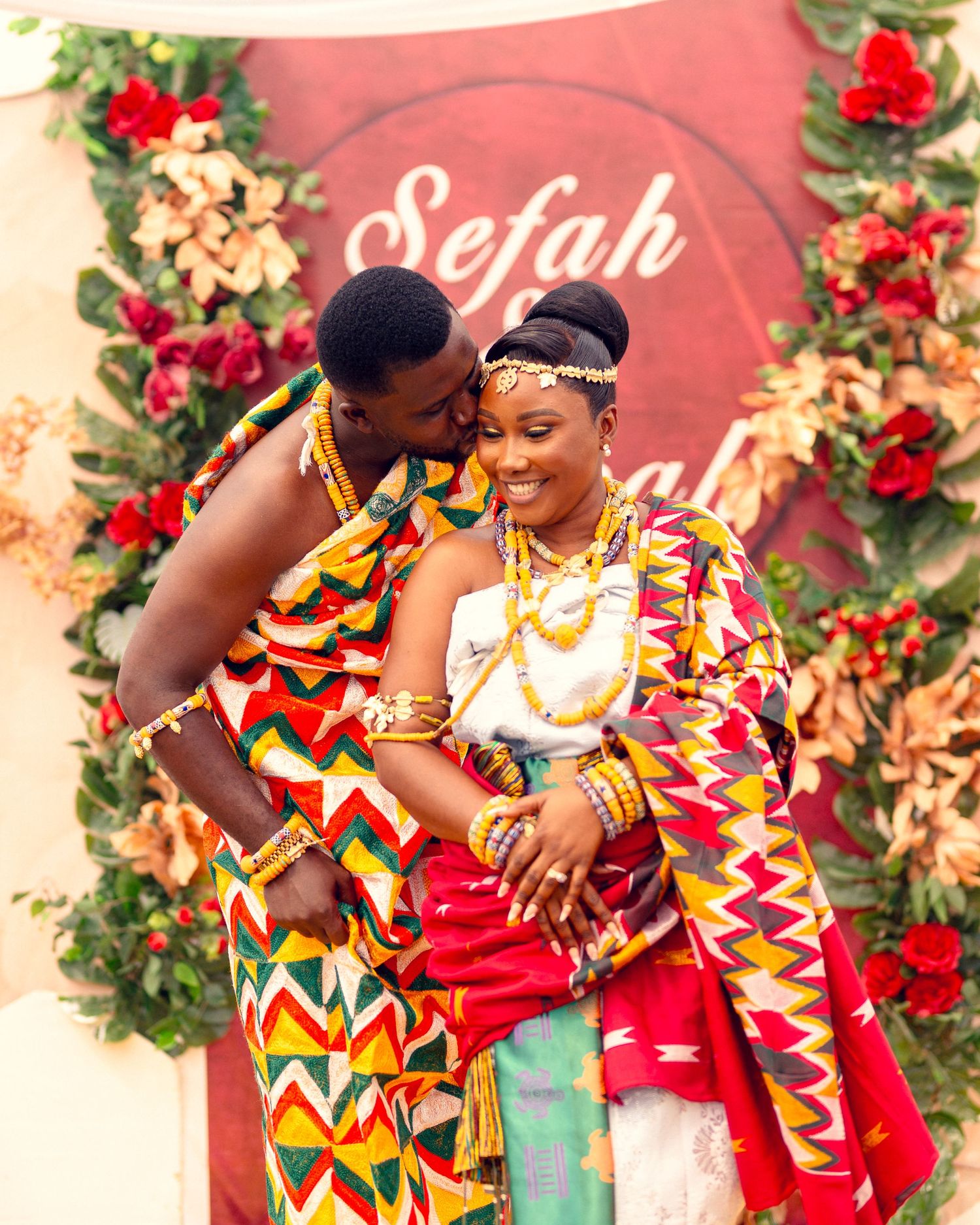 Romantic moment captured against red floral wall with Sefah signage in traditional African attire.