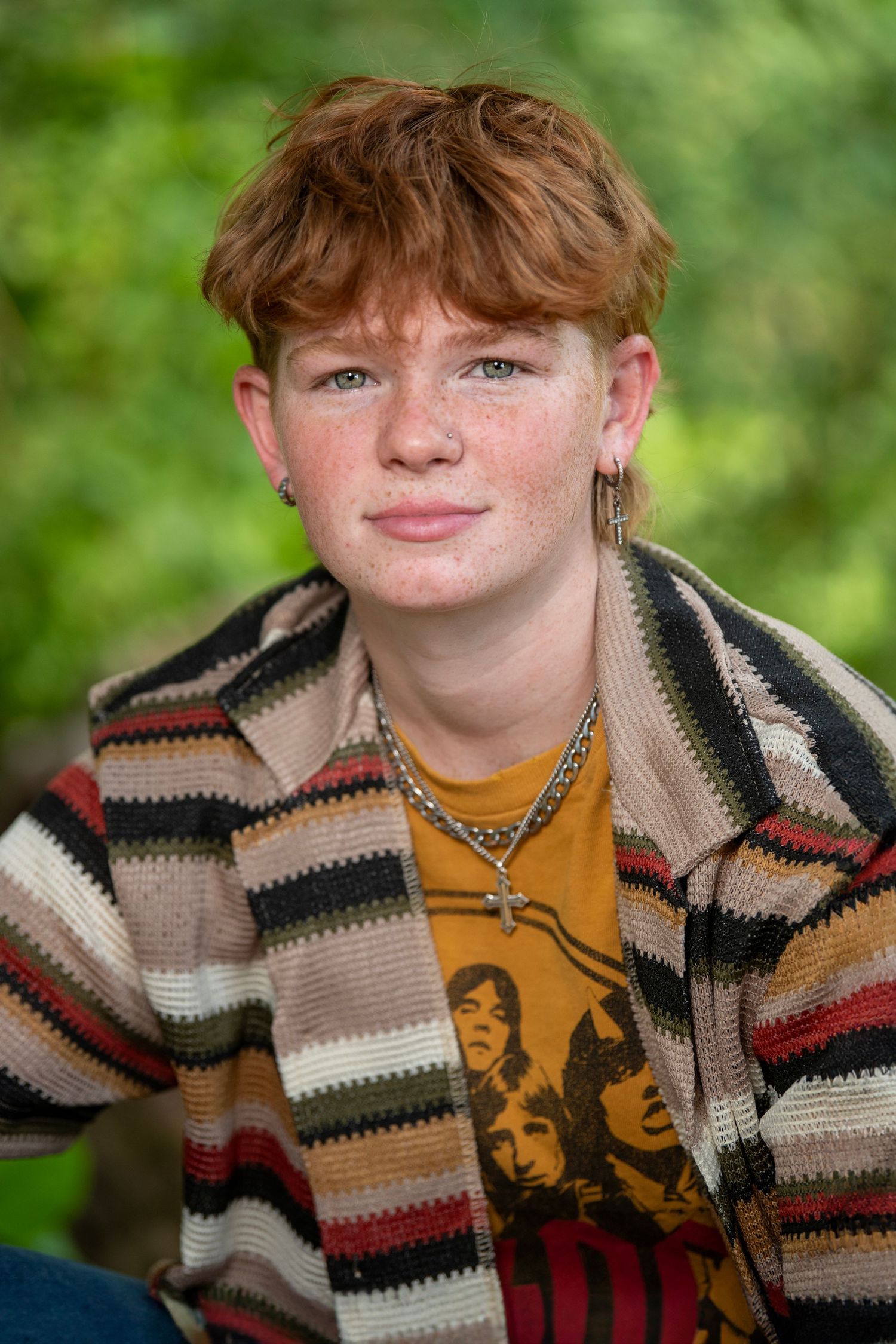 Portrait photo of someone wearing a striped knit cardigan and yellow graphic t-shirt against a blurred green background.