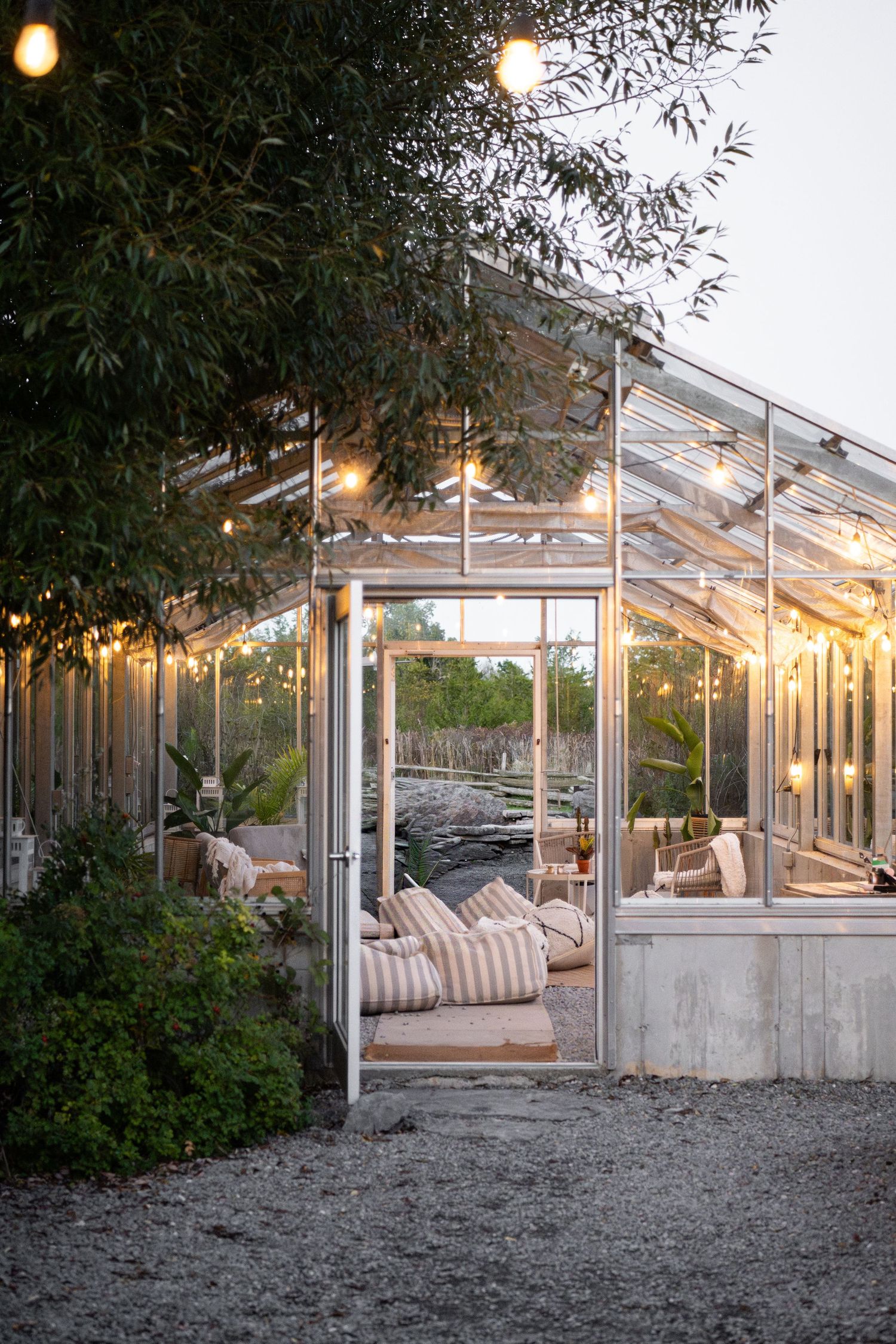 Glass greenhouse with string lights and cozy lounge seating at dusk.