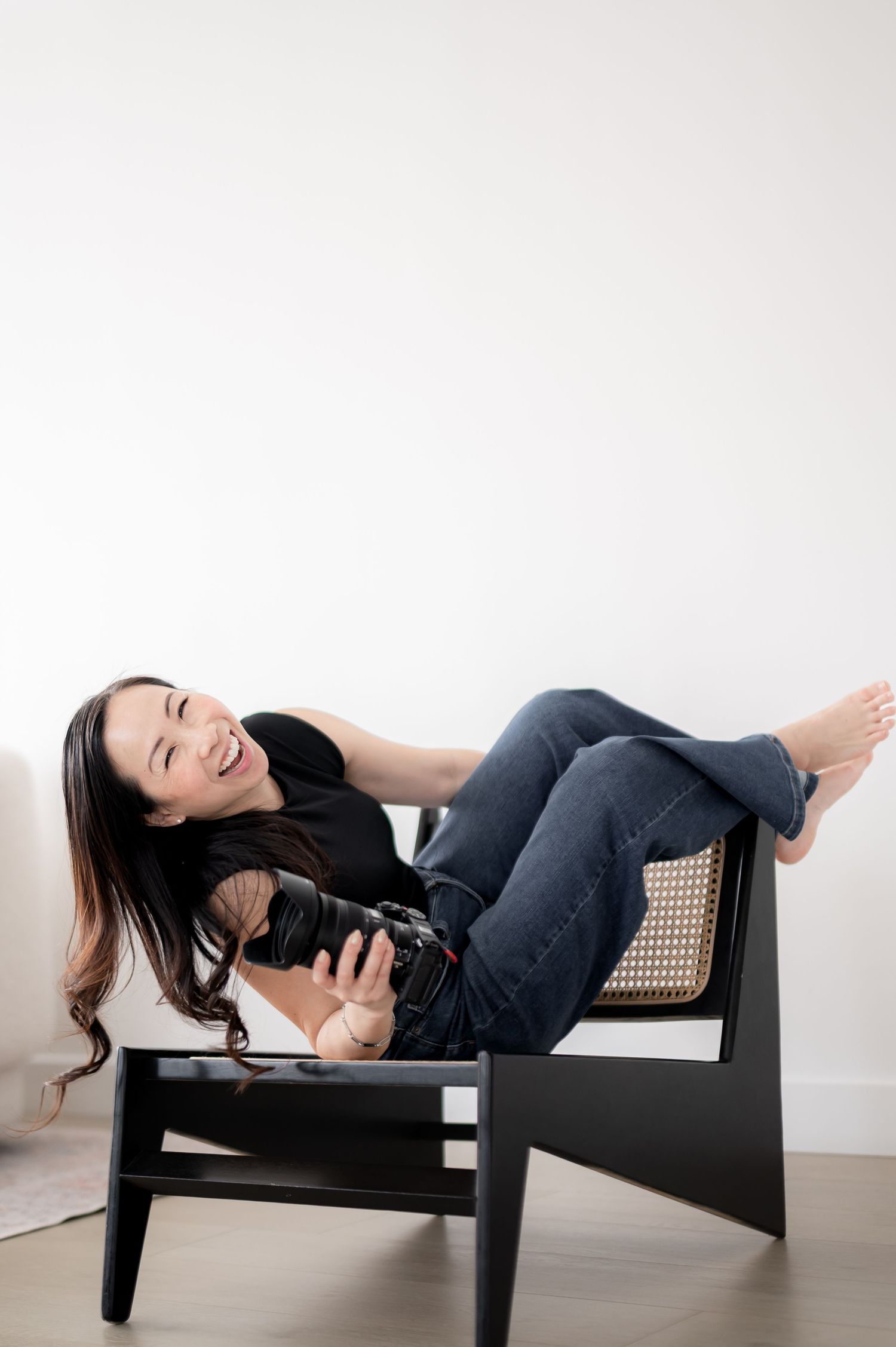 Photographer using professional camera lens while wearing cozy cream sweater for self portrait in soft lighting.