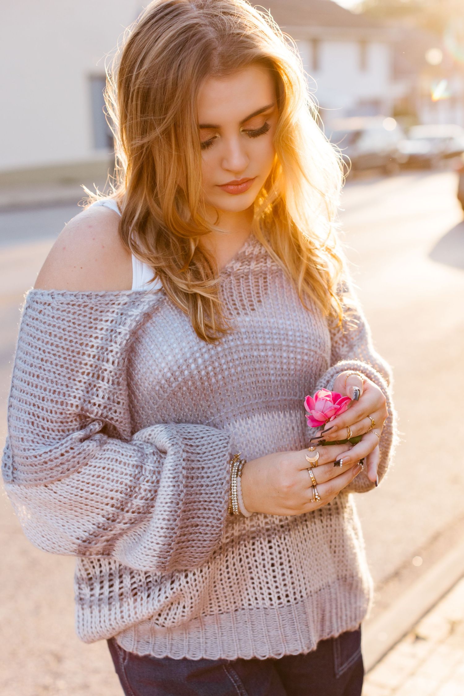 Woman in cozy gray knit sweater looking down at phone in warm sunlight during golden hour.