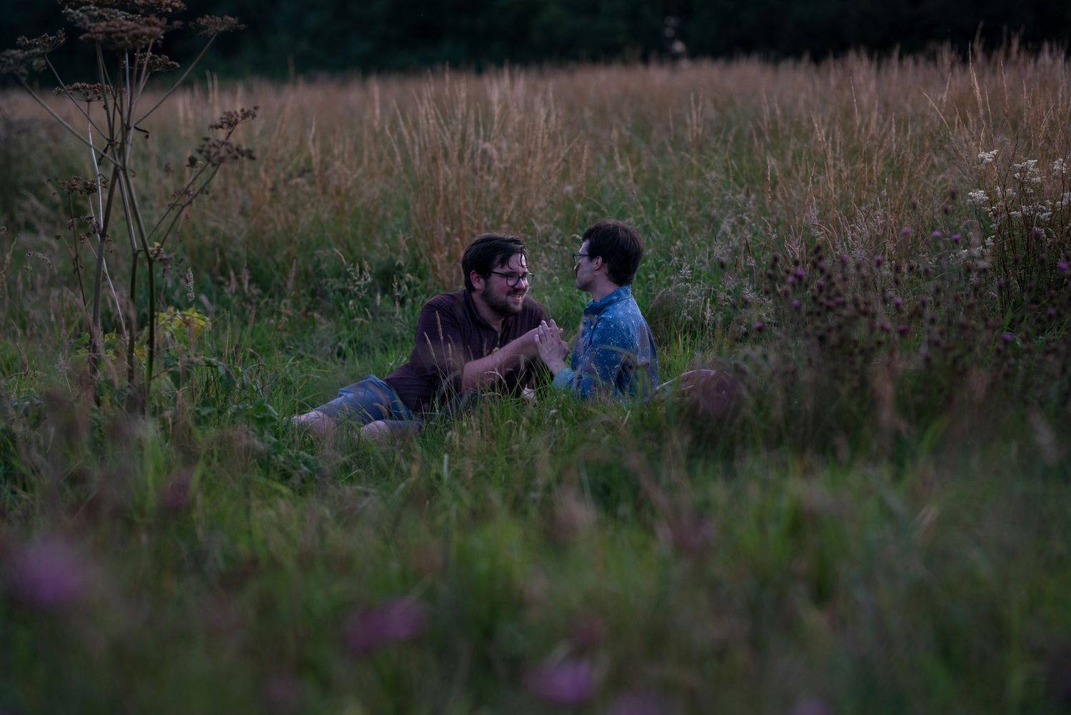 Couple sharing an intimate moment outdoors in a natural field setting at sunset.
