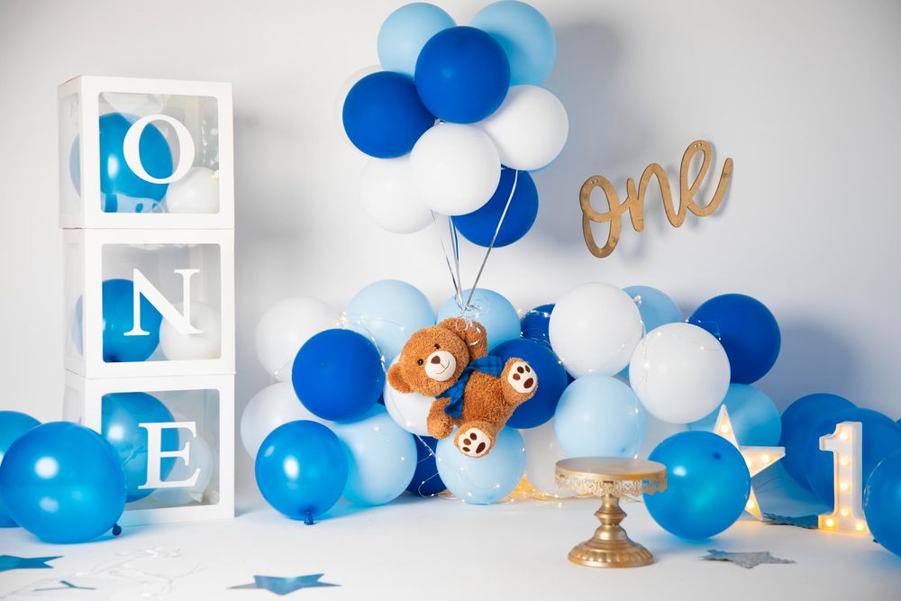 First birthday party decor with blue balloons, teddy bear, and ONE letter boxes.