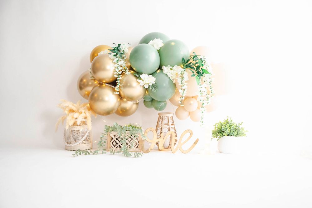 Gold and sage green balloon garland with floral accents above ONE letters for a first birthday party setup.