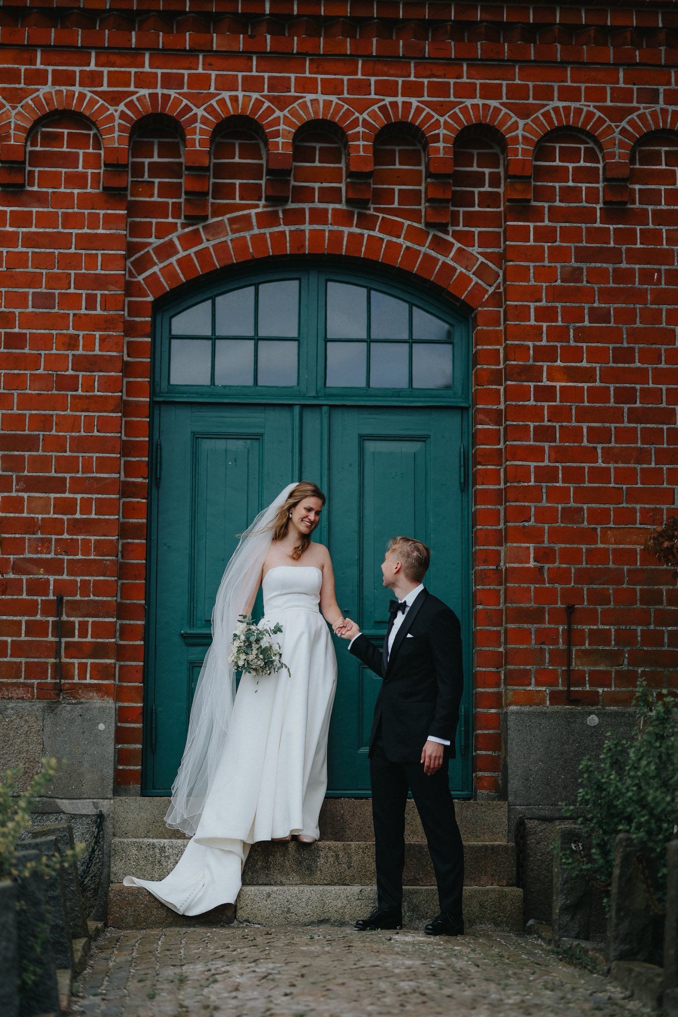 Wedding couple shares romantic moments against rustic brick wall with teal doors in four candid photo sequence.