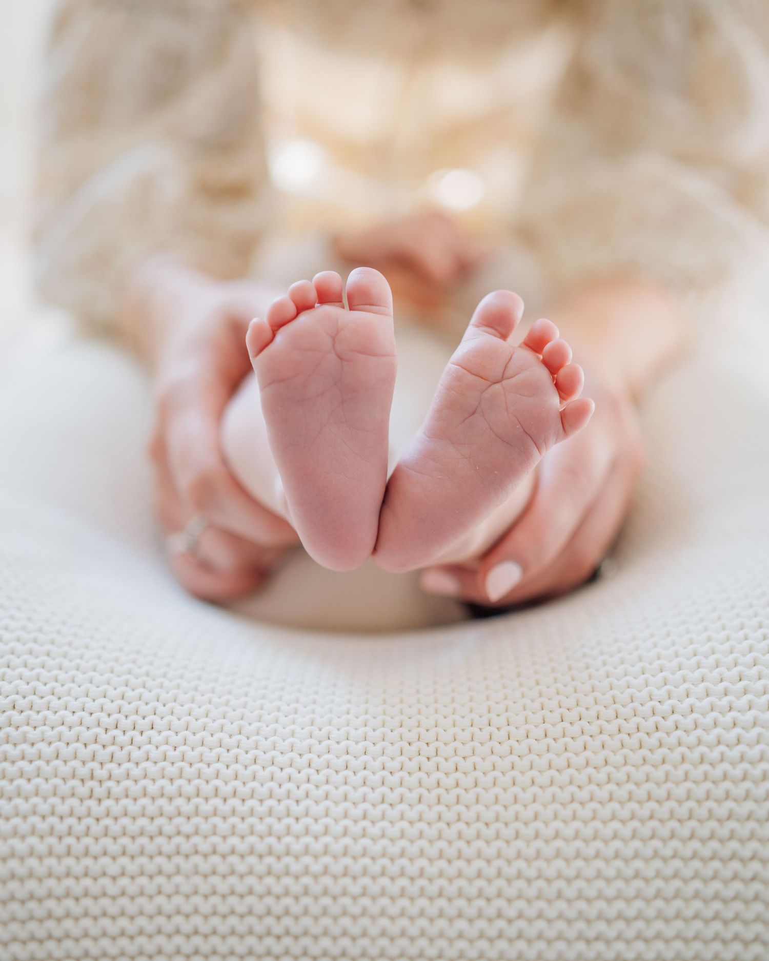 Close up of tiny newborn baby feet being held against white knitted fabric.